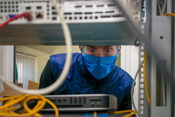 Portrait of a teenager in a data center. A technician in a medical mask works in a rack with...
