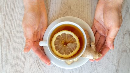 Cup of tea with lemon and ginger in hands close-up on a light background. Alternative medicine to SARS-CoV-2 virus. Food protection against viruses, coronavirus, immunity concept.