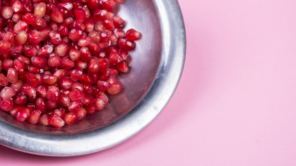 Pomegranate grains in a metal plate and half ripe pomegranate on a pink background
