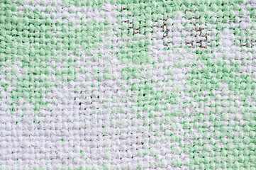 Closeup texture of a roughly painted white and light green canvas lying on a wooden surface. Background for fabric texture. Universal background.