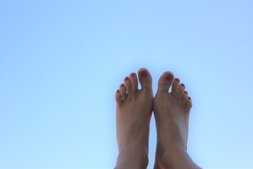 female feet with red pedicure on a background of blue sky