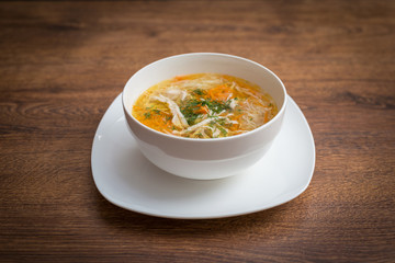 Homemade chicken noodle soup in pot with carrots, celery, topped with parsley bits.