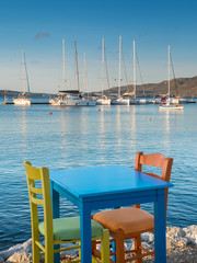 Fototapeta na wymiar blue table with two chairs and sea view to yacht marine in Greece