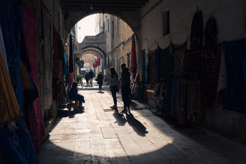 Calle estrecha con siluetas de gente y alfombras colgadas en las paredes en la medina de Essaouira