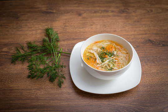 Homemade chicken noodle soup in pot with carrots, celery, topped with parsley bits.