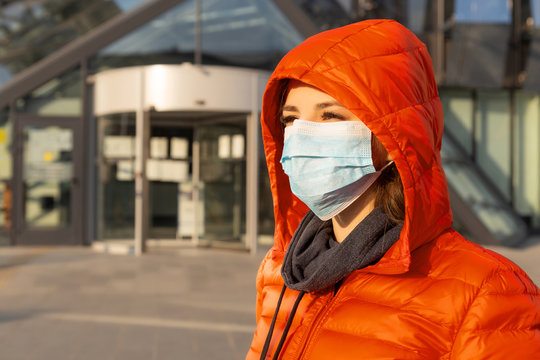 A woman wears a protective mask against allergies, viruses, air pollution. Climate change concept. Portrait of a young woman in a medical mask from a coronavirus in a red jacket on the street.