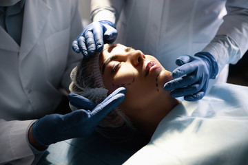 Doctor and nurse preparing female patient for cosmetic surgery in clinic