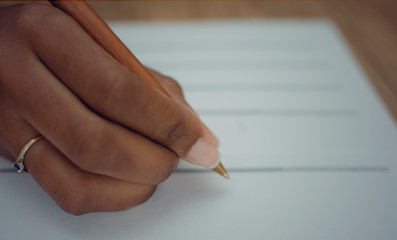 Closeup of the right hand of a black woman filling a paper document.  Selective focus on her index finger.