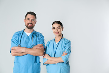 Mature doctor and young nurse against light background