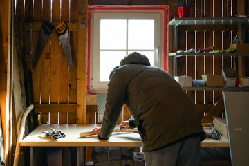 Process of man making wooden walking stick indoors during quarantine. Carving wood stick on the table using knife