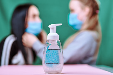 disinfectant fights bacteria. a daughter wearing a blue medical mask dresses her mom 's mask. green background pink table. covid-19. protect the health