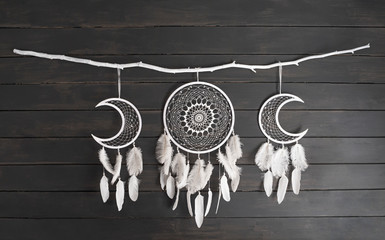 White dream catcher with feather hanging at black wooden background