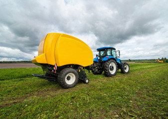 blue tractor with baler in motion at field at agro work