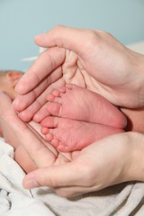 a small newborn baby in the arms of its mother, the mother holds the newborn's legs in her hands