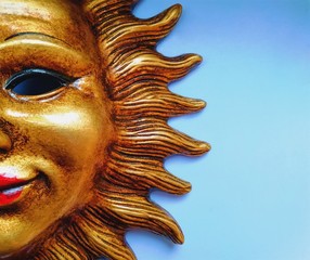 part of a decorative gilded mask, resembling the sun, on a light blue background