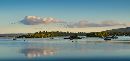 Panoramic landscape of a sunset on a lake in Ireland with clouds reflected in the water.
