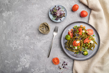Tagliatelle green spinach pasta with tomato, pea and microgreen sprouts on a gray concrete background. Top view, copy space.