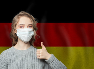 Happy woman in face mask holding thumb up on national flag Germany  background. Flu epidemic and...