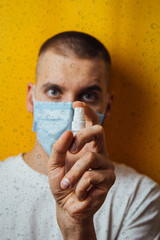 Portrait of a young guy in a mask on a yellow background. Disinfects hands with an antiseptic. Sprays the pest control. The concept of coronavirus. Protection against germs and viruses.