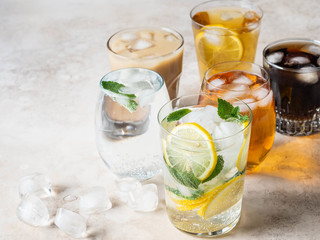 Various refreshing drinks in glasses with ice. Apple juice, cola, homemade lemonade, iced coffee, iced fruit tea and sparkling water on a beige background. Copy space
