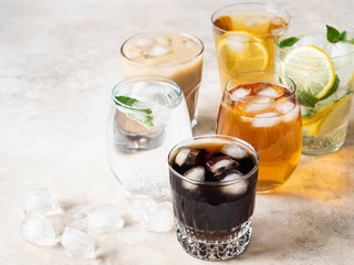 Various refreshing drinks in glasses with ice. Apple juice, cola, homemade lemonade, iced coffee, iced fruit tea and sparkling water on a beige background. Copy space