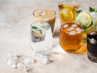Various refreshing drinks in glasses with ice. Apple juice, cola, homemade lemonade, iced coffee, iced fruit tea and sparkling water on a beige background. Copy space