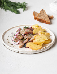 Marinated Herring fish with potatoes slices and red onion, rye bread on the white table.