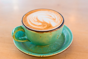 One cup of cappuccino with latte art on wooden background, greenery ceramic cup, place for text