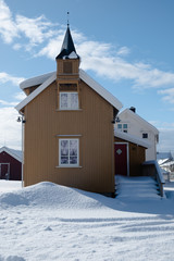 Fototapeta na wymiar Cozy scandinavian house with belfry in city Svolvaer. Located in Lofoten Islands. House in yellow color is covered by snow. 
