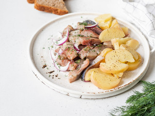 Marinated Herring fish with potatoes slices and red onion, rye bread on the white table.