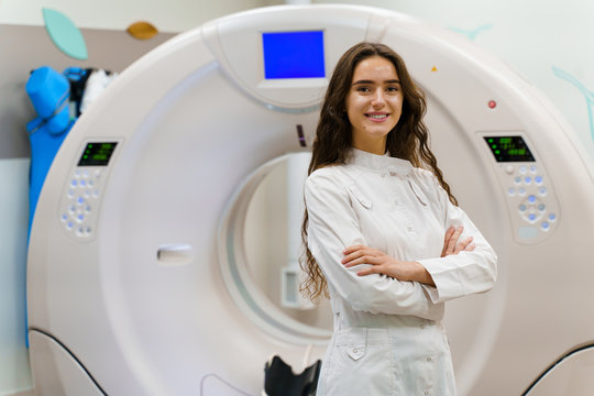 The Young Women Doctor In Medical Gown Looks In Camera. Patient After Computer Tomography. CT Diagnostic In Medical Clinic