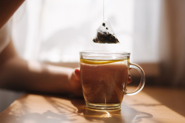 Hand of woman making black tea with lemon on wooden table