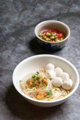 Rice stick noodles with fish ball and garlic cracklings with lard in white bowl; pickled chilli condiment on table.