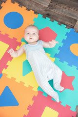 Laughing child on a colored rubber mat puzzle for playing foam with geometric figures