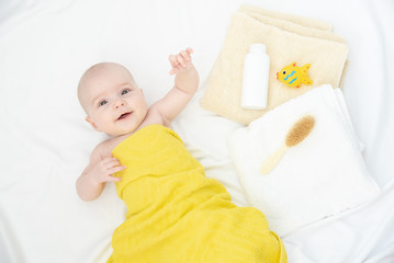Portrait of a beautiful cheerful baby in a yellow towel after bath on a white cloth