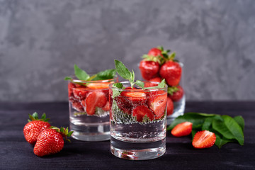 Infused water with strawberry and mint in sparkling glasses on wood black table background, copy space. Cold summer drink. Mineral water