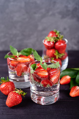 Infused water with strawberry and mint in sparkling glasses on wood black table background, copy space. Cold summer drink. Mineral water