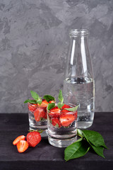 Infused water with strawberry and mint in sparkling glasses on wood black table background, copy space. Cold summer drink. Mineral water