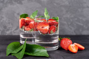Infused water with strawberry and mint in sparkling glasses on wood black table background, copy space. Cold summer drink. Mineral water