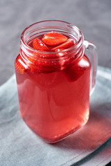 Homemade strawberry tea with in mason jar on gray napkin, copy space. Cold summer berry drink in sparkling glasses. Fresh vitamin beverage