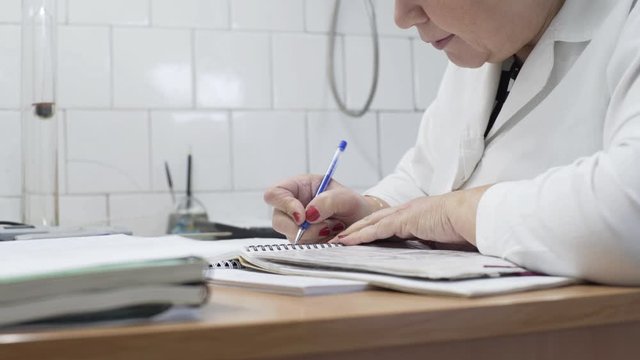 Lab researcher writing research report. Female researcher in lab. Closeup of lab scientist hand writing notes. Woman hand writing science report