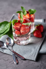 Water with strawberry and mint in sparkling glasses on gray napkin on concrete table, copy space. Cold summer drink. Mineral water