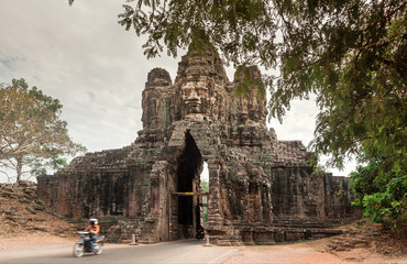 Motorcycle driving through the gate of Angkor with Buddha face, Great City of 12th century