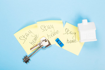 Concept of self-isolation and quarantine. Stay at home. White house, toy car, keys and sticker with text on blue background