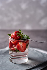 Water with strawberry and mint in sparkling glasses on gray napkin on concrete table, copy space. Cold summer drink. Mineral water