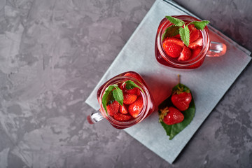 Homemade strawberry tea with mint in mason jar on gray concrete table background, copy space. Cold summer berry drink in sparkling glasses. Fresh vitamin beverage