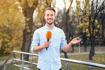 Young male journalist with microphone working in park