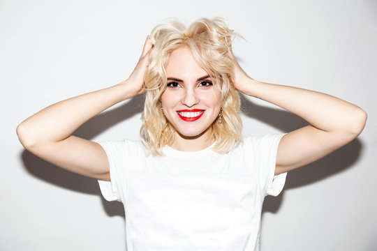 young happy smiling blonde girl with beautiful makeup in a white t-shirt on a white background, studio fashion photo