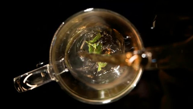 Black tea is poured into a glass cup on a black background
