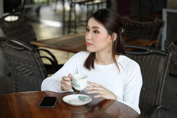 Young asian woman sit at rustic cafe holding cup drink coffee look around